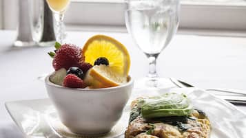 A breakfast setting with a bowl of fruit, a glass of orange juice, a glass of water, and a plate with a pastry.