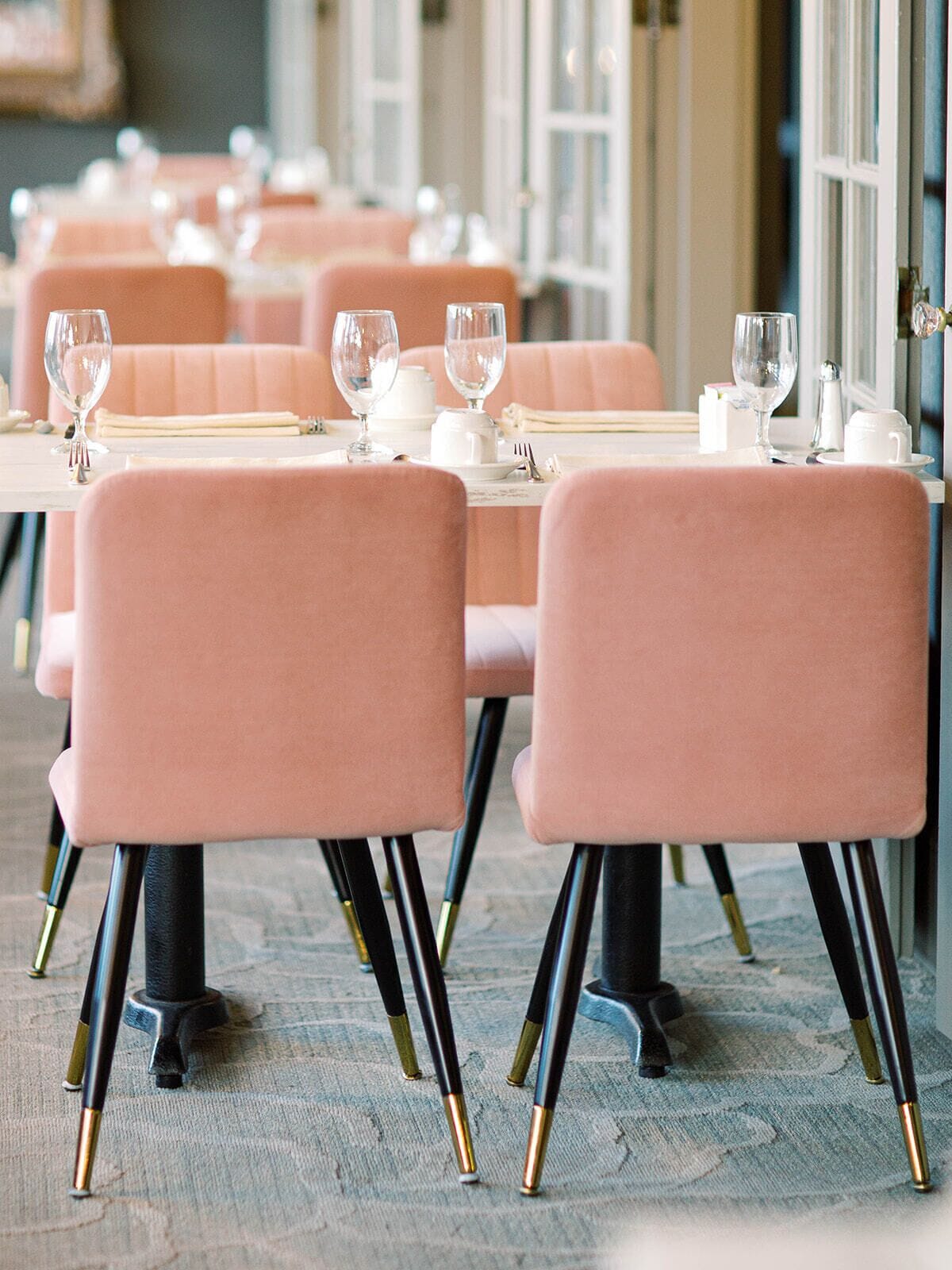 A restaurant with pink upholstered chairs and tables, each set with wine glasses and cutlery.