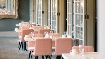 A dining area with tables and chairs, large windows, and a mirror on the wall.