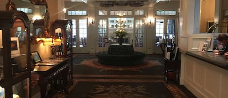 A grand lobby with a chandelier, a reception desk, and a patterned carpet.