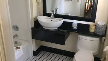 A bathroom with a white sink, black countertop, and a large mirror. There is a toilet and a shower area visible.