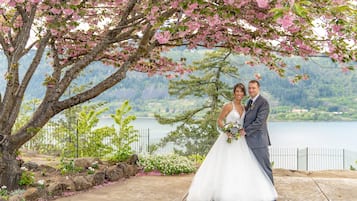 A wedding couple standing under a blooming tree by a lake.