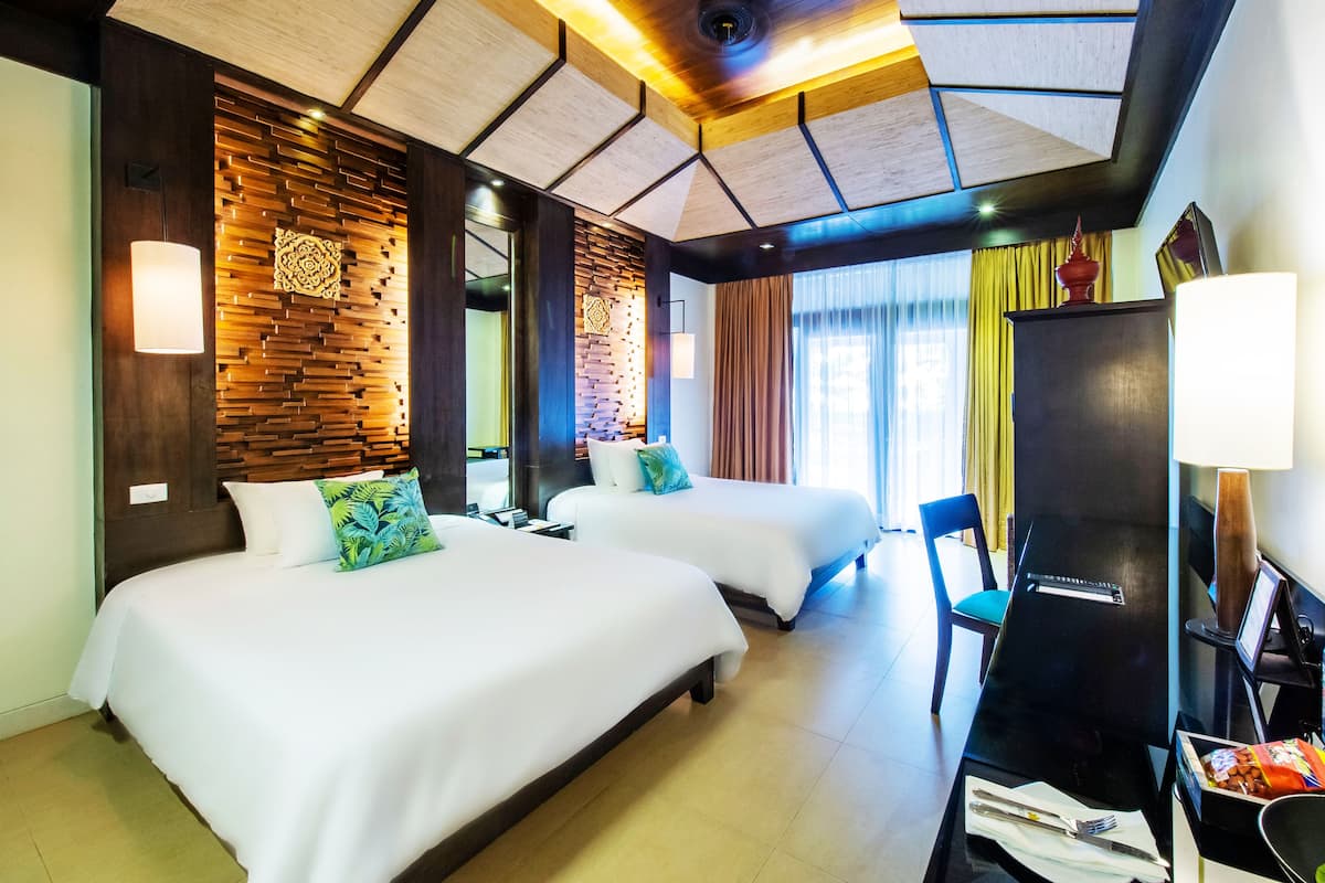 Quarto de hotel com duas camas, uma escrivaninha, uma cadeira, uma televisão e um painel de parede com padrão geométrico.