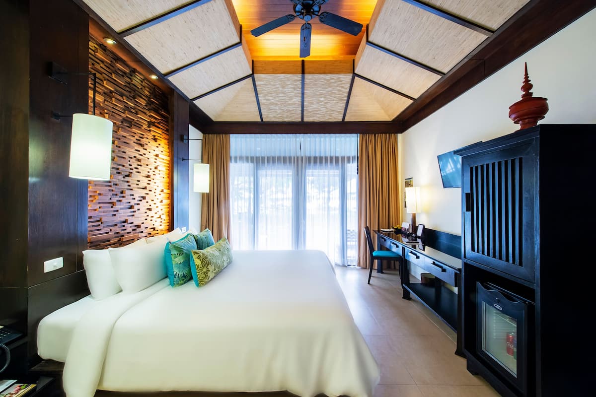 Quarto de hotel com uma cama grande, uma escrivaninha, uma televisão e um ventilador de teto.