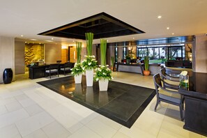 A spacious lobby with a reception desk, seating area, and large windows offering views of the outdoors.