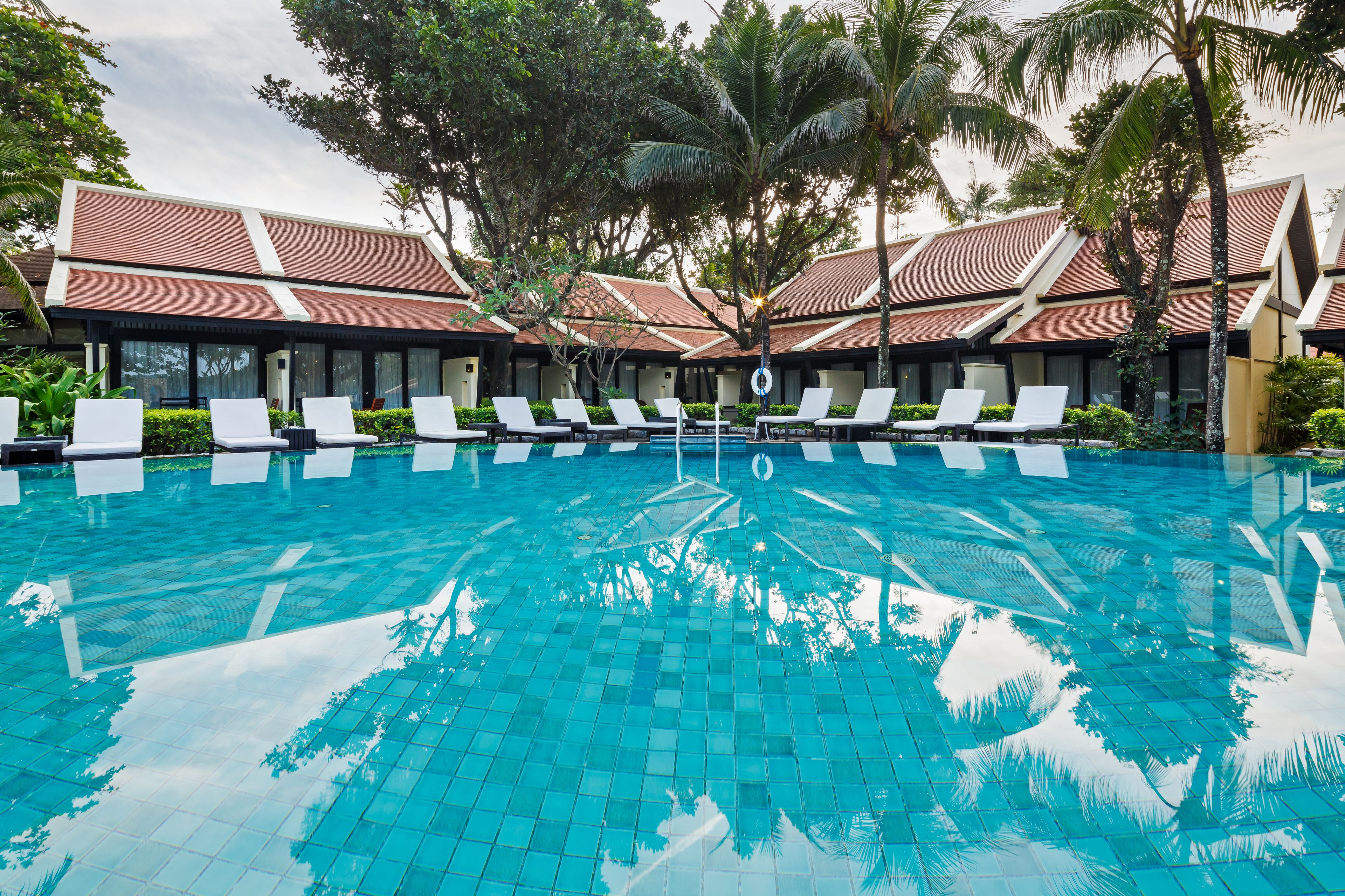 Une piscine avec des chaises longues et un bâtiment doté d’un toit en tuiles.