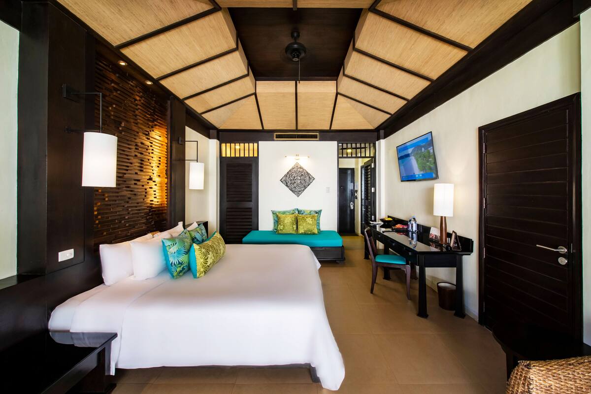Quarto de hotel com uma cama grande, uma escrivaninha, uma cadeira, uma televisão e um guarda-roupa.