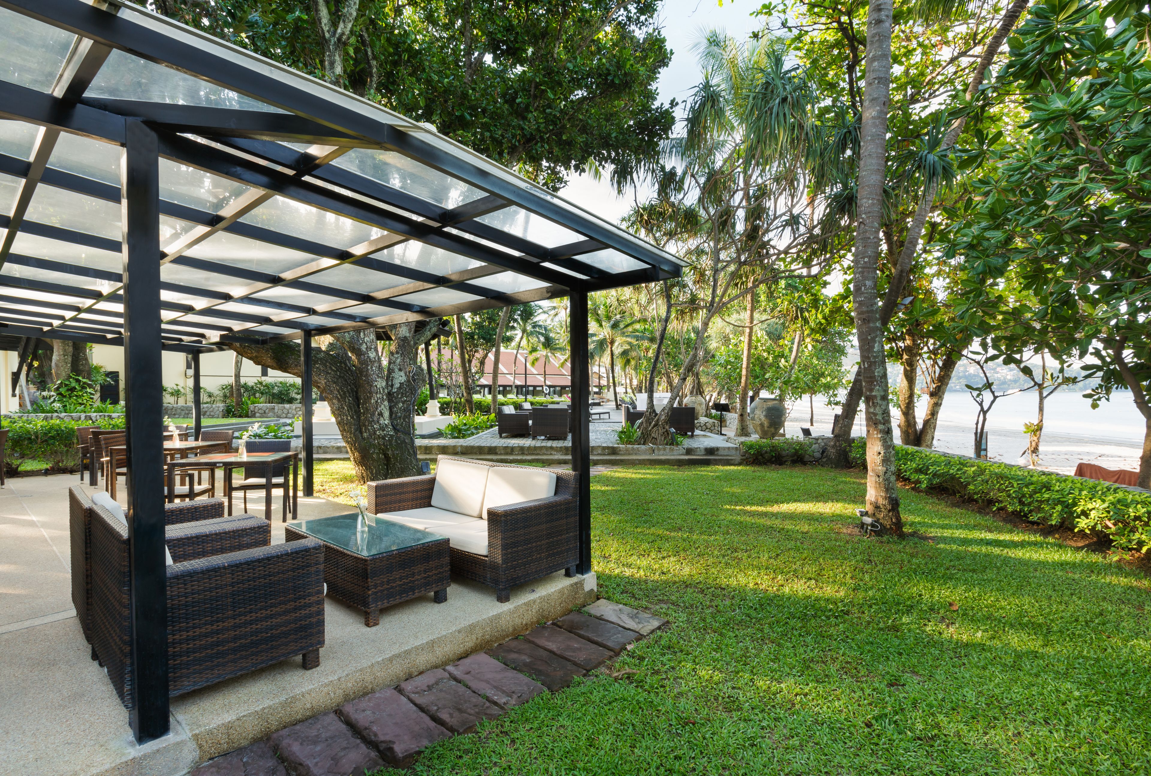 An outdoor patio area with wicker furniture, a glass-top table, and a pergola structure.