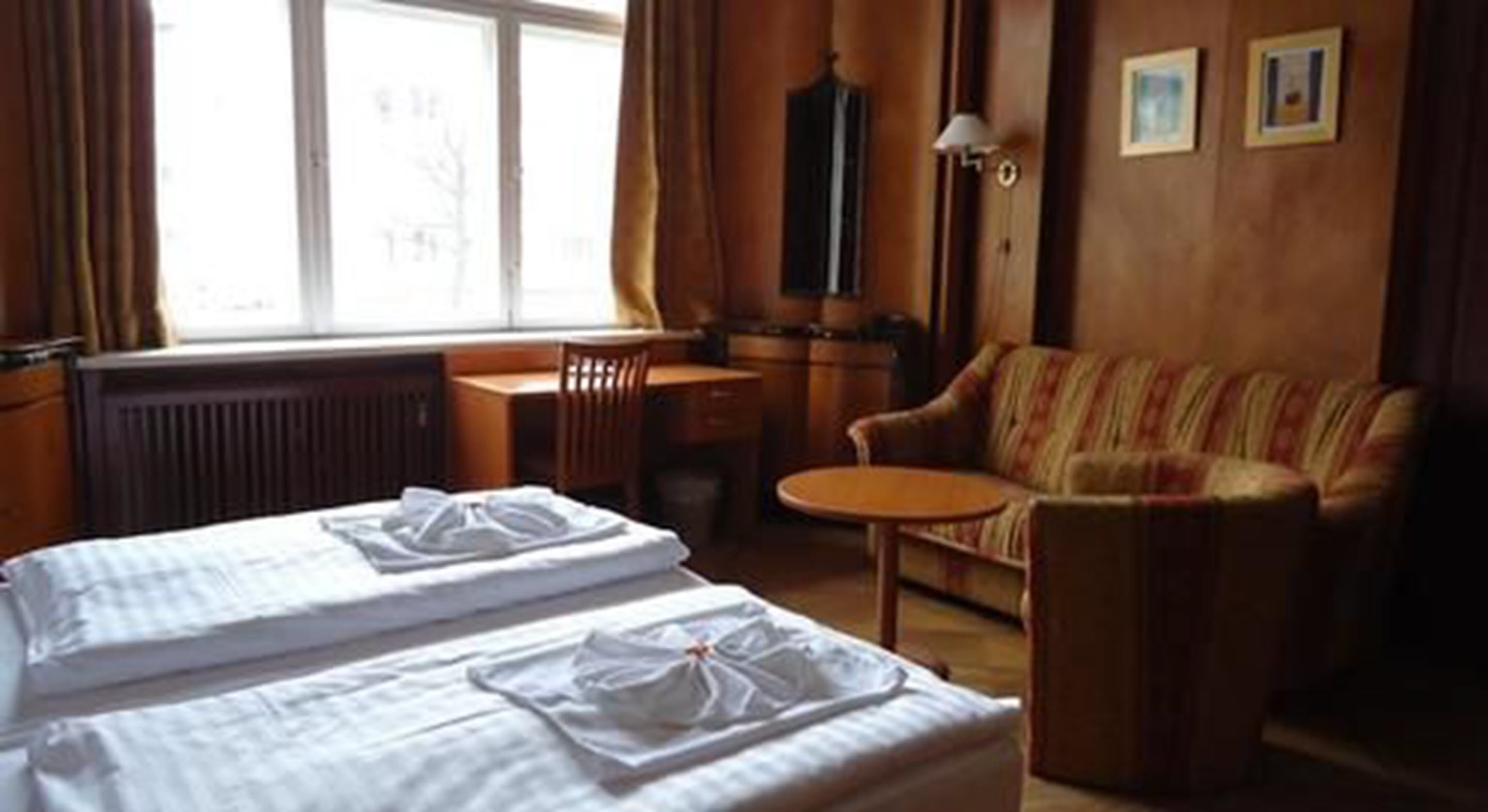 A hotel room with two beds, a sofa, a small table, and a window with curtains.