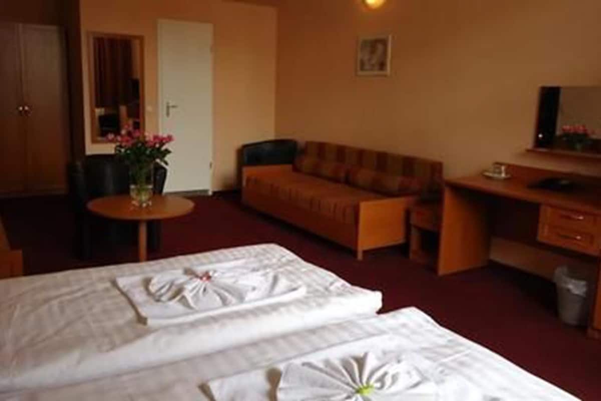 A hotel room with two beds, a sofa, a desk, a chair, and a small table with a vase of flowers.