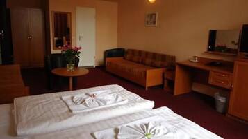 Habitación de hotel con dos camas, un sofá, un escritorio, una silla y una mesita con un jarrón de flores.