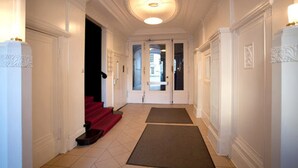A hallway with white walls, a red carpet, and a door leading to another room. - Hotel Aster (Berlin)