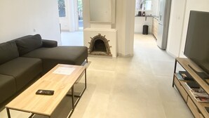 Uma sala de estar moderna com um sofá, uma mesa de centro, lareira, televisão e uma área de cozinha ao fundo.