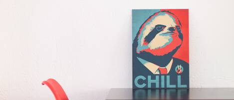 A dining table with a red and green chair, a framed artwork with the word "CHILL" on it, and a white wall in the background.