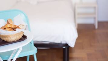 A bedroom with a bed, a bedside table, a chair, and a basket of bread.