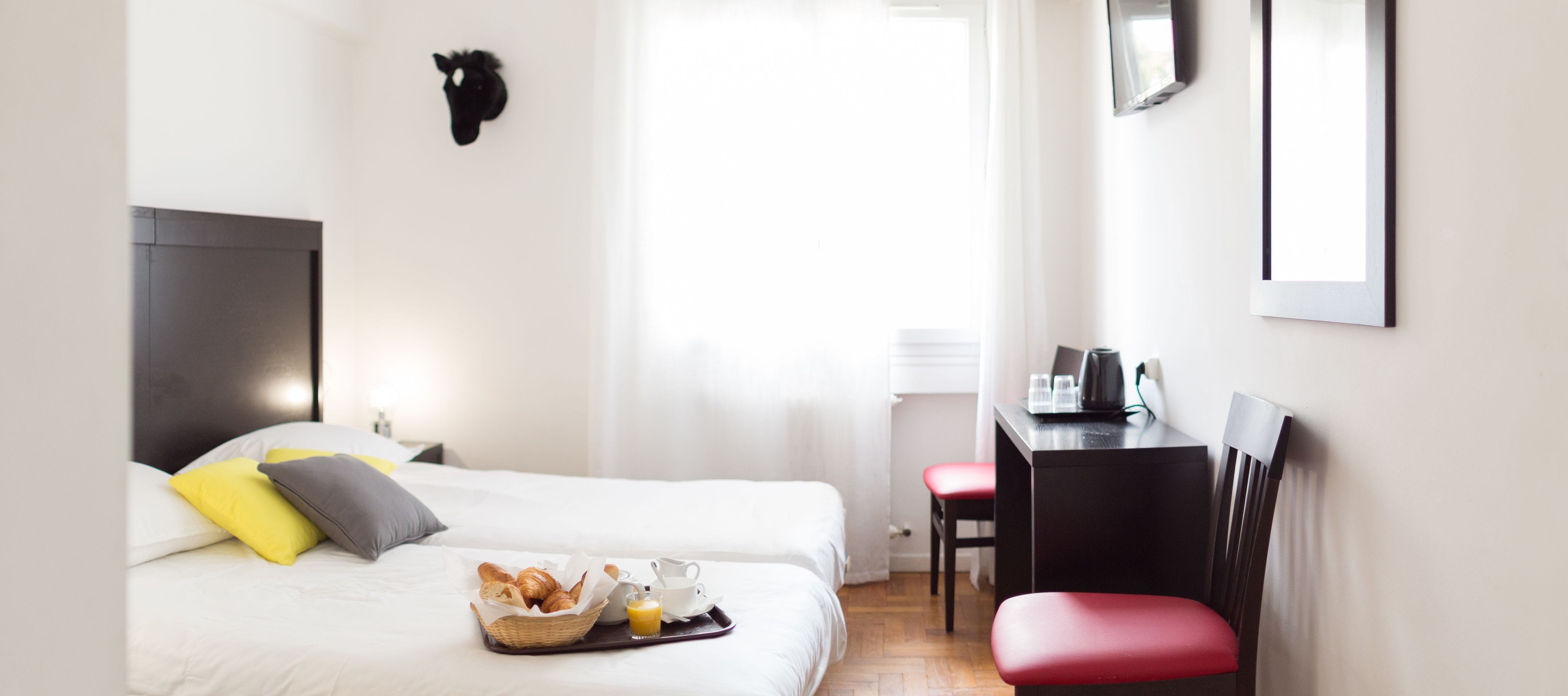 A hotel room with a bed, breakfast tray, desk, chair, and a mounted animal head on the wall.