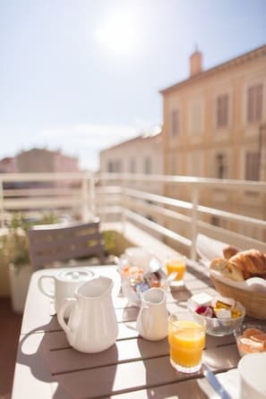 A breakfast table with a pitcher, jug, and glass of orange juice, set on a balcony with a railing and buildings in the background. - Hotel Esperanto (Cannes)