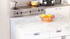 Uma cozinha com bancada branca, micro-ondas, fogão e uma cesta de frutas.