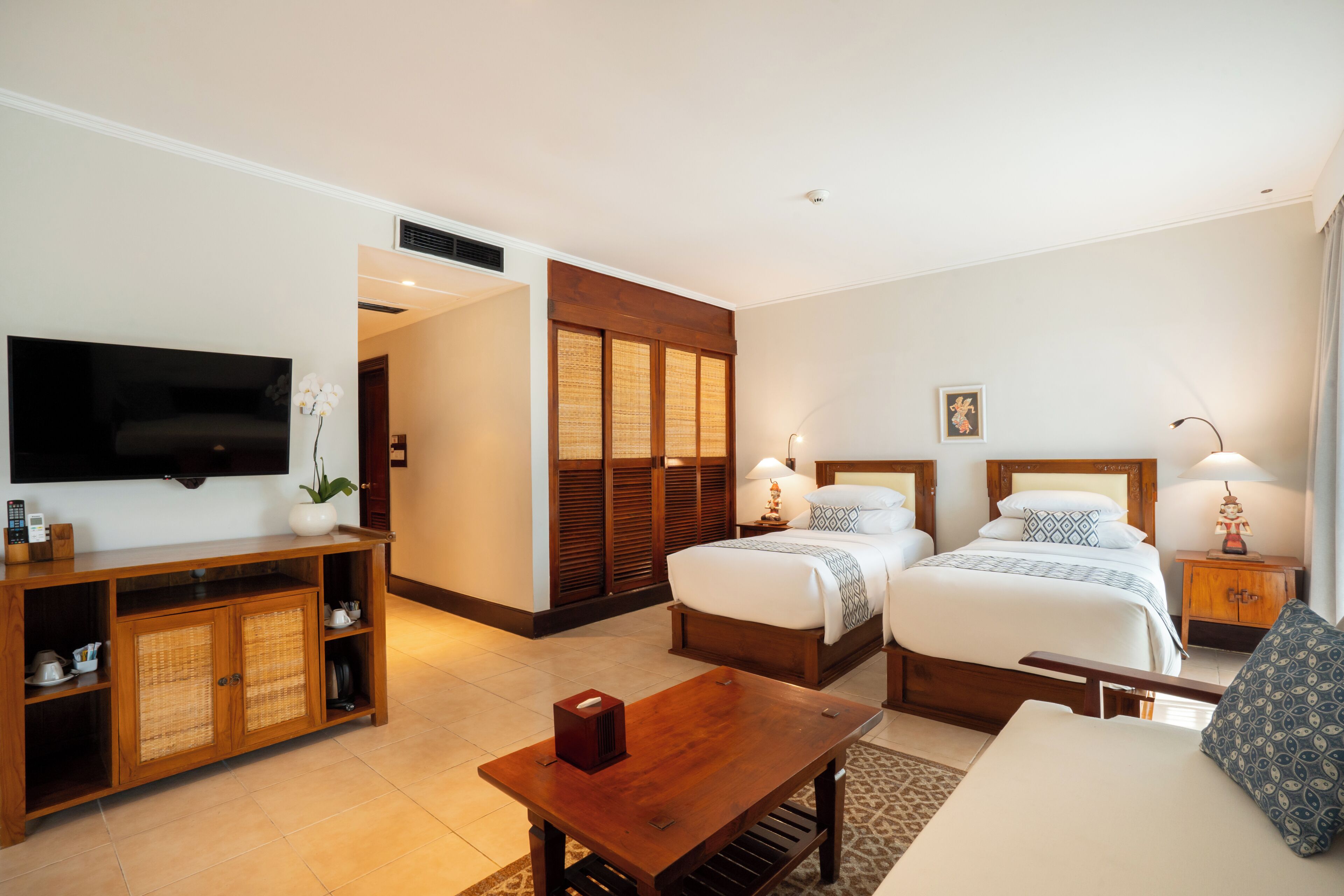A hotel room with a TV, two beds, a wooden cabinet, a table, and a lamp.