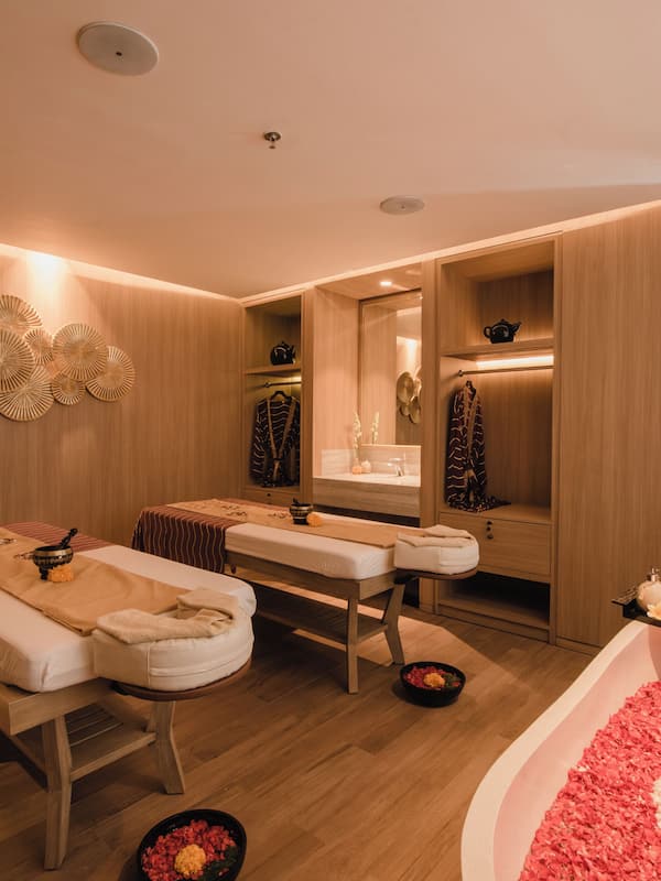 Relax in a serene spa room with two massage tables, a bathtub filled with rose petals, and a peaceful ambiance.