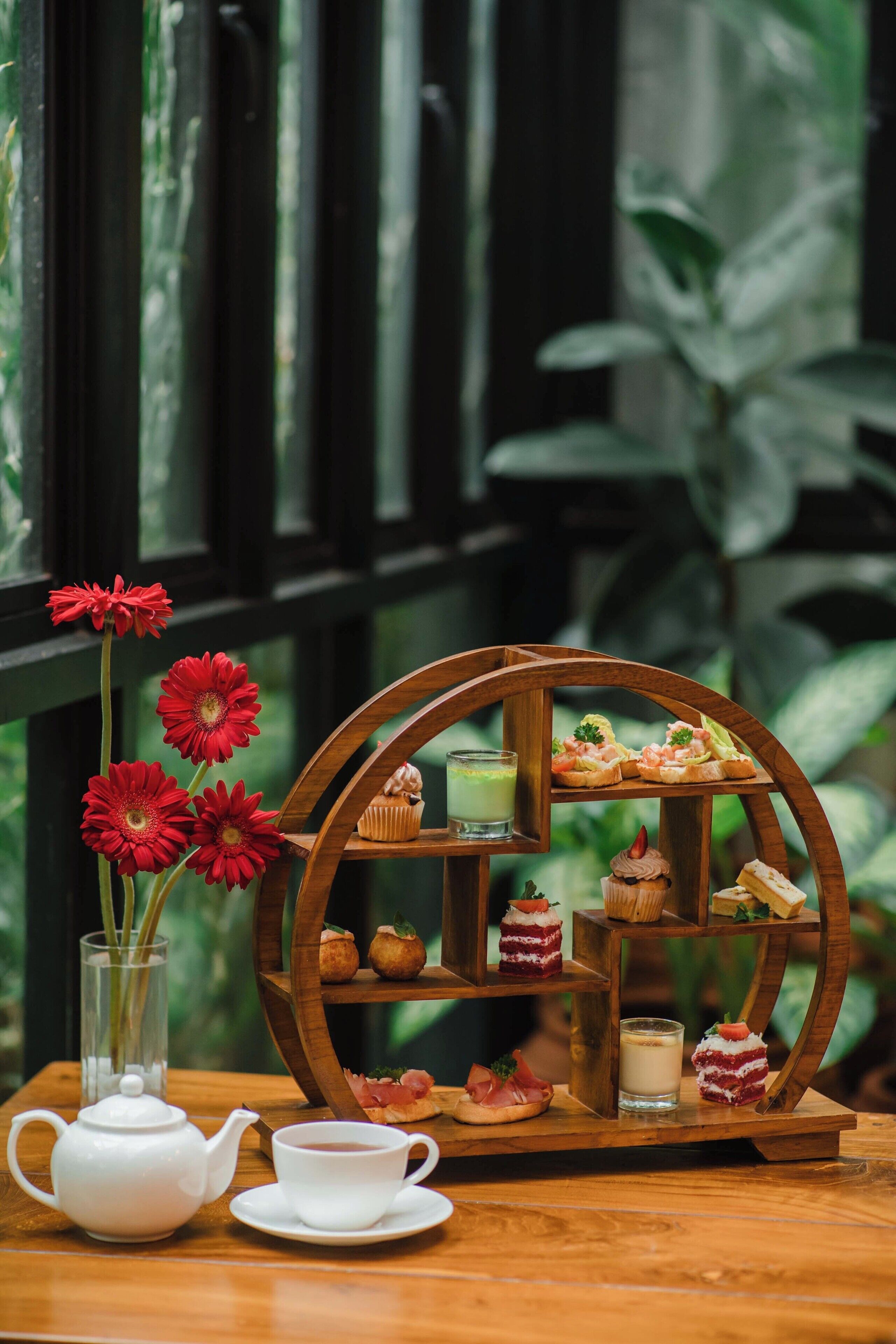 A wooden table with a teapot, cup, and a tiered tray of pastries.