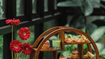 A wooden table with a teapot, cup, and a tiered tray of pastries.