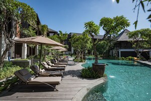 A poolside area with lounge chairs and umbrellas, surrounded by lush greenery and a clear blue pool.