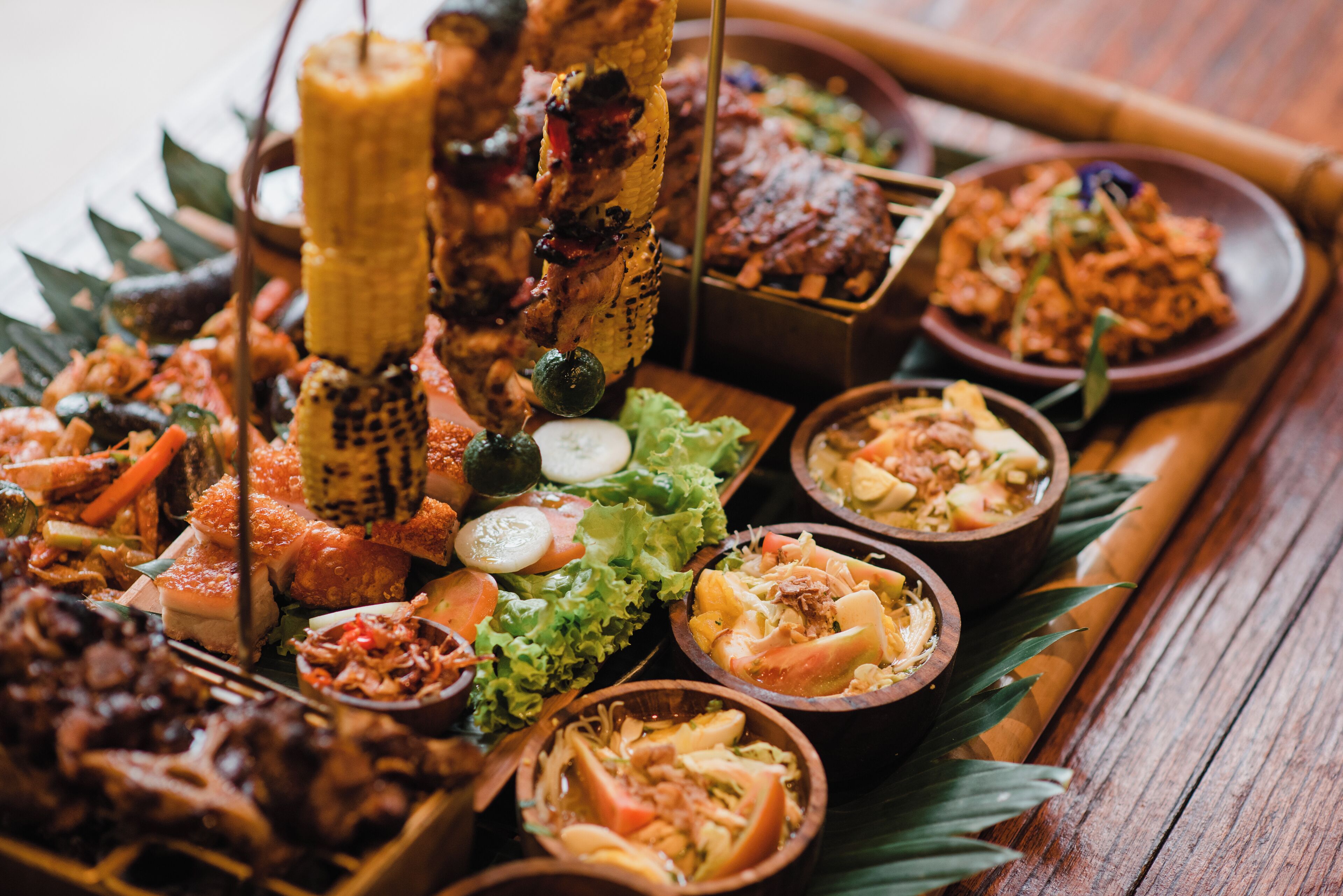 A variety of dishes arranged on a wooden table, including grilled meats, vegetables, and rice dishes.