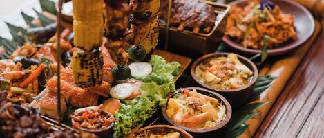 A variety of dishes arranged on a wooden table, including grilled meats, vegetables, and rice dishes.