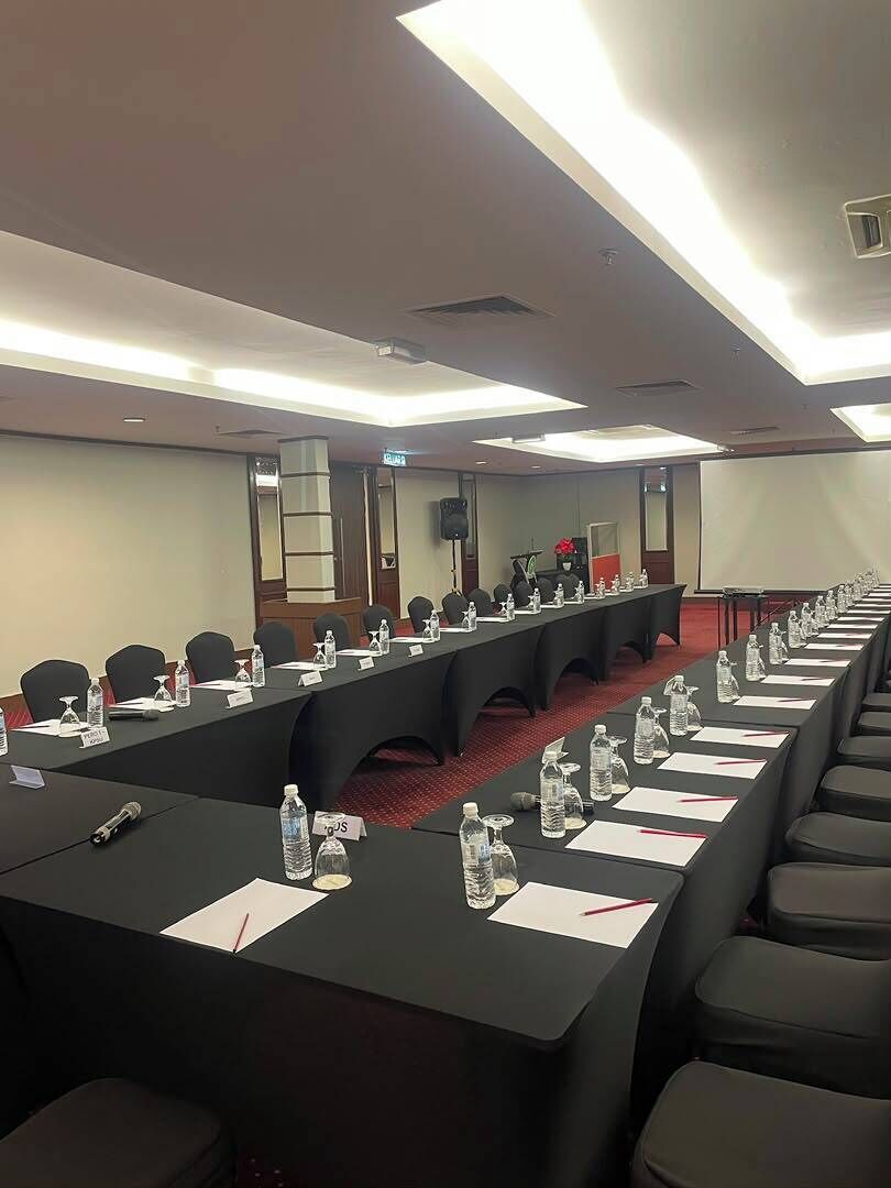 A conference room with a long table, chairs, nameplates, water bottles, and a projector screen.