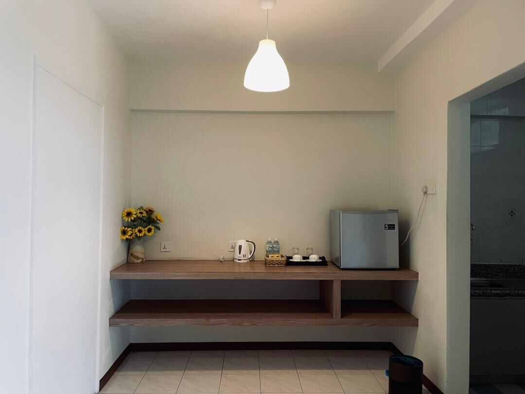 A small kitchenette with a built-in refrigerator, a coffee maker, and a shelf with a vase of sunflowers.