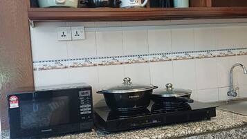 Cozinha com micro-ondas, duas bocas elétricas, chaleira e panela numa prateleira de madeira.