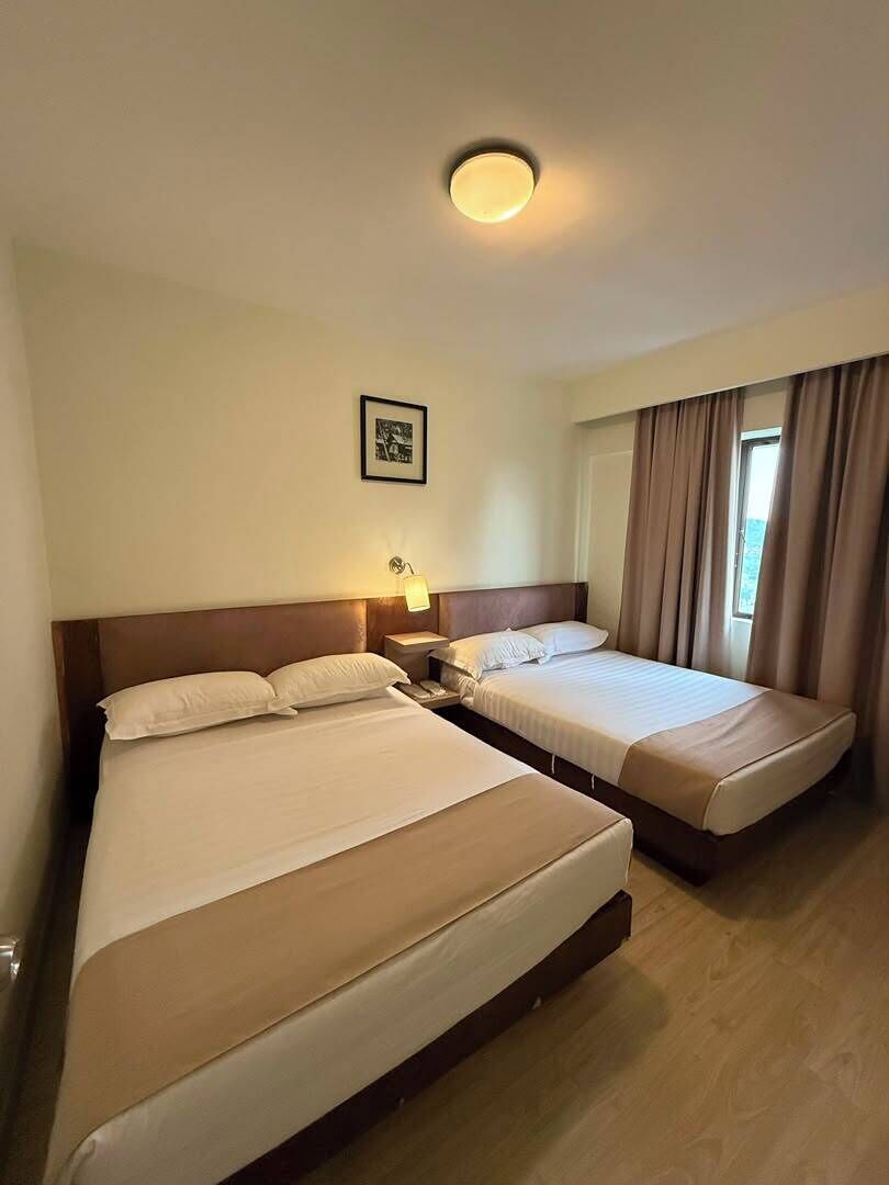 Une chambre d’hôtel avec deux lits, une table de chevet avec une lampe, un tableau encadré au mur et une fenêtre avec des rideaux.