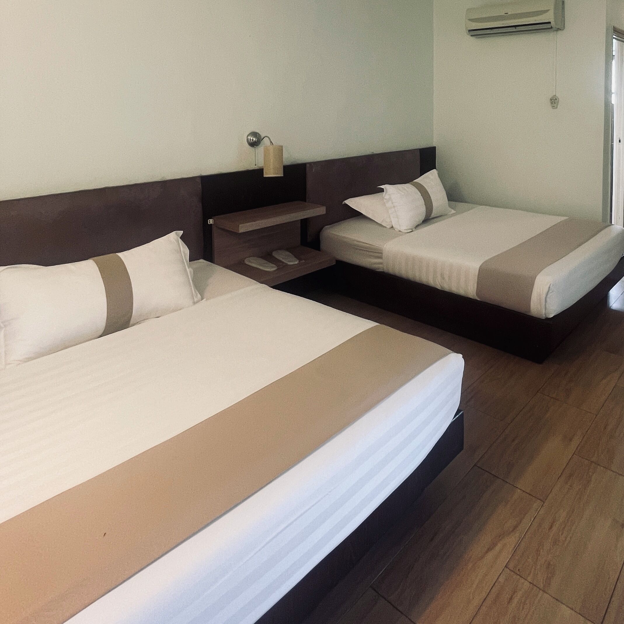 A hotel room with two beds, a nightstand, a shelf, and an air conditioning unit.