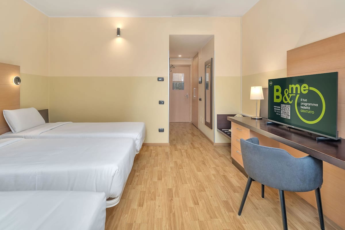 A hotel room with two beds, a desk, a chair, and a television displaying a program.