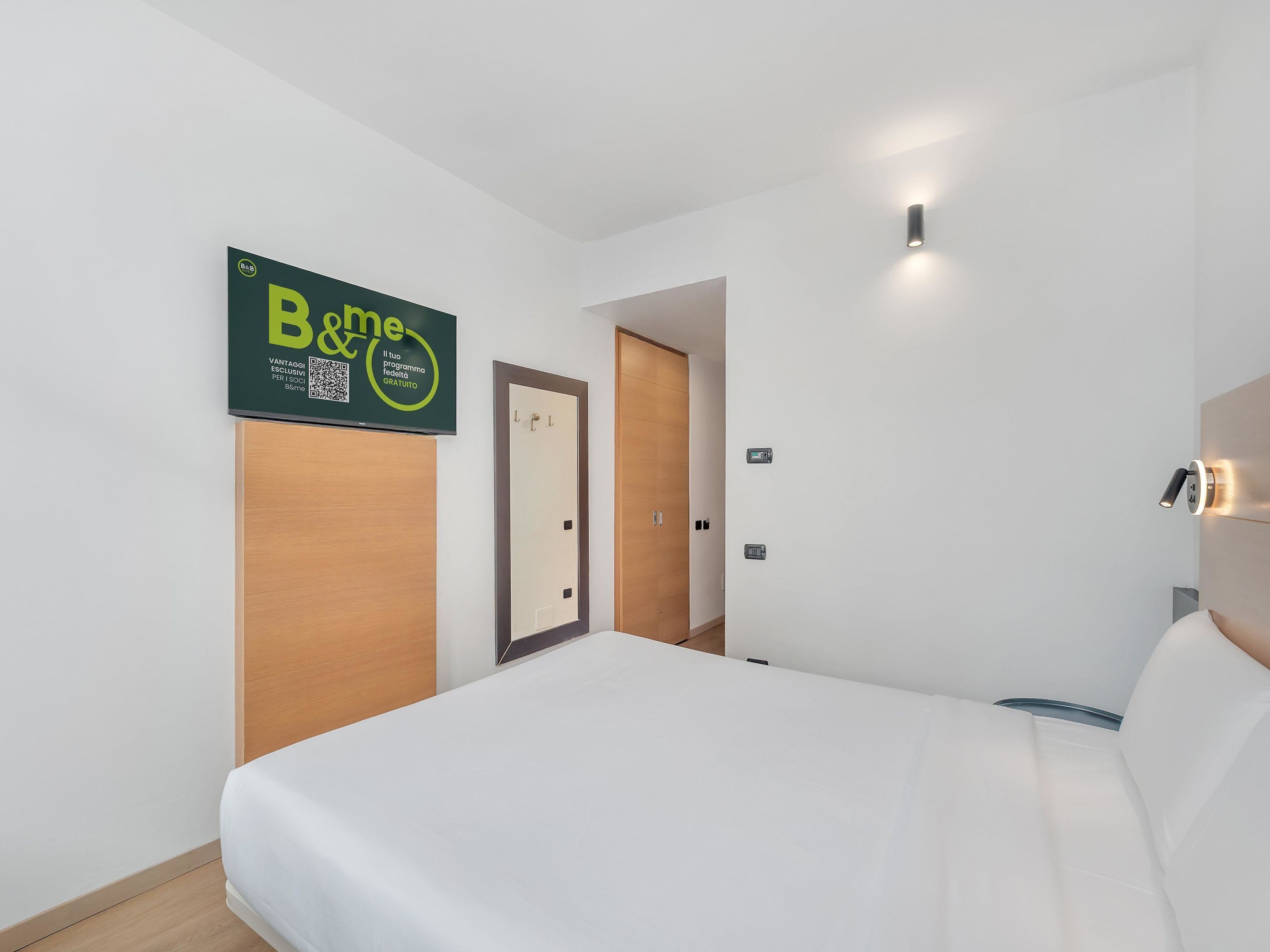 Ein modernes Hotelzimmer mit Bett, Holzschrank, Tür und einem Schild an der Wand.