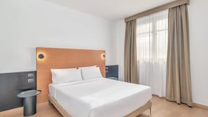 Een moderne hotelkamer met een houten hoofdeinde, een groot bed, een nachtkastje en een raam met gordijnen.