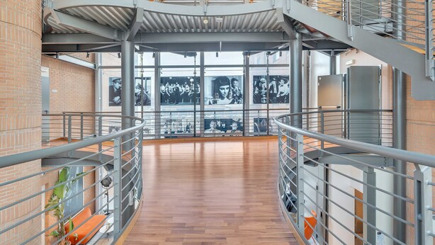 Een ruim interieur met een hoge plafond, metalen hekwerk en een houten vloer.