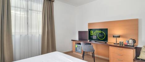 Ein Hotelzimmer mit einem Bett, einem Schreibtisch mit Computer, einem Fernseher und einer Kaffeemaschine.