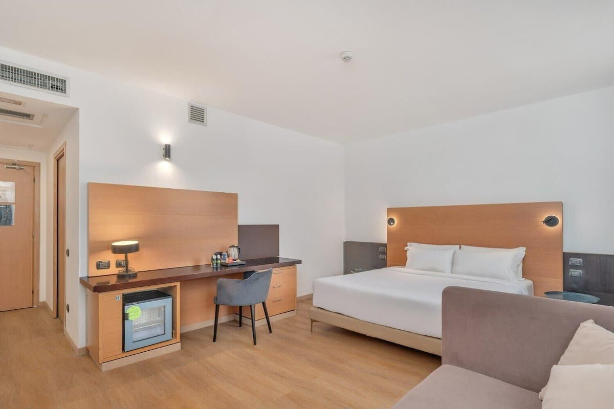 A hotel room with a bed, a desk with a chair, a small kitchenette, and a sofa.