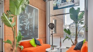 Een moderne lounge met oranje banken, grote potplanten en een groot raam met uitzicht op de stad.