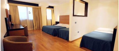 A hotel room with two single beds, a desk with a chair, a TV, and a large mirror on the wall.