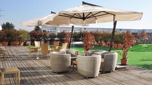 An outdoor deck with wicker furniture, a large umbrella, and potted plants. - Golf Hotel Milano (Opera)