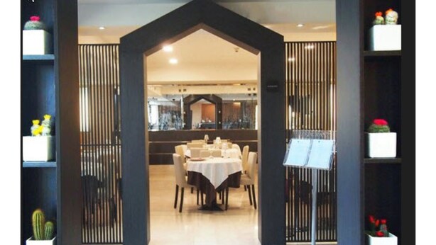 A restaurant with a central dining area, a black-framed entrance, and potted plants on shelves. - Golf Hotel Milano (Opera)
