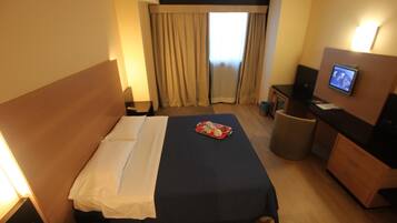 Une chambre d’hôtel équipée d’un lit, d’un bureau avec un ordinateur, d’une télévision et d’une petite poubelle.