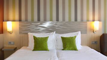 Habitación de hotel con una cama grande, dos almohadas, cabecera con lámpara y pared a rayas.