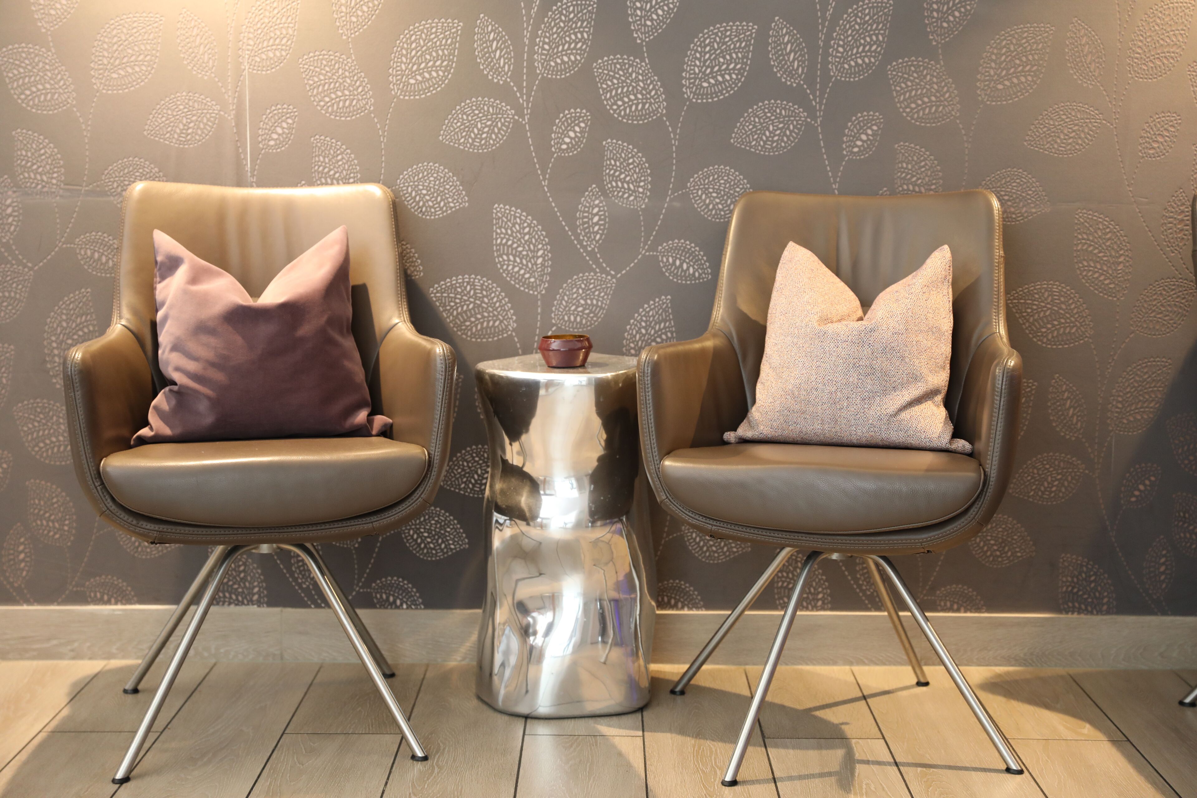 Two leather armchairs with cushions, a small metallic side table, and a patterned wallpaper.