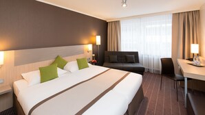 A hotel room with a large bed, a sofa, a desk, and a chair. - New Orly (Munich)