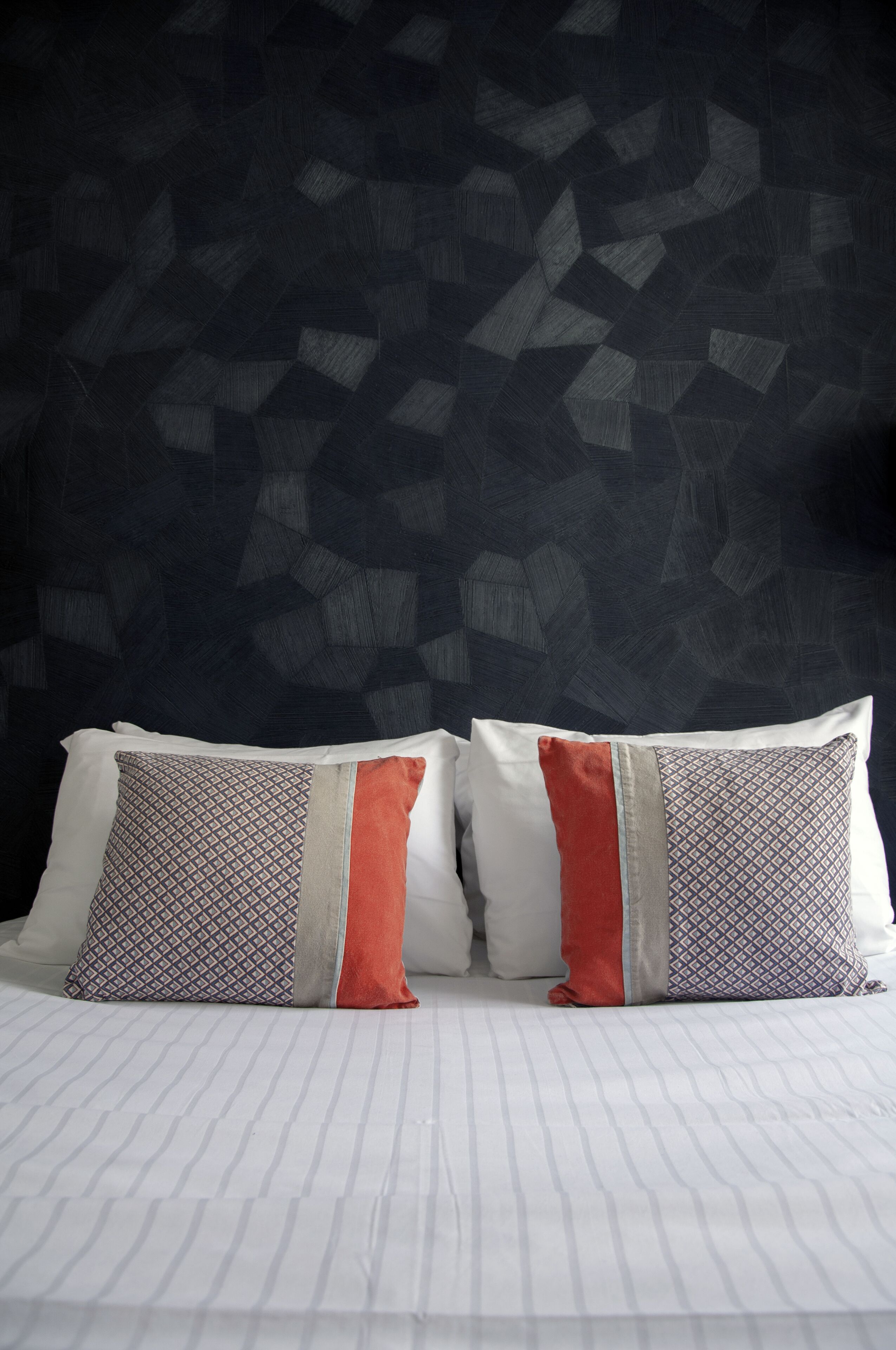 A bed with striped bedding and two pillows with geometric patterns and a red accent.