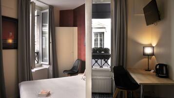 A hotel room with a bed, a desk, a chair, a TV, and a window with curtains.